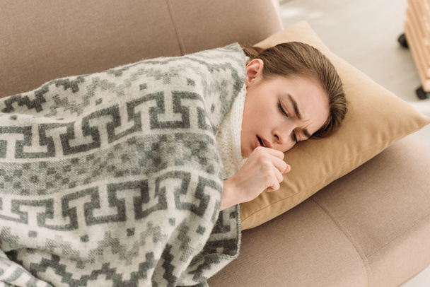chica enferma tosiendo mientras está acostada en el sofá debajo de la manta
 - Foto, Imagen