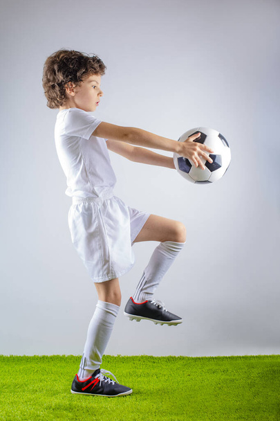 Full profile length shot of a little soccer player juggling a football isolated on gray background - Zdjęcie, obraz