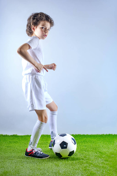 Little boy footballer in presenting and points a finger at a free space on a light background. Copy space - 写真・画像
