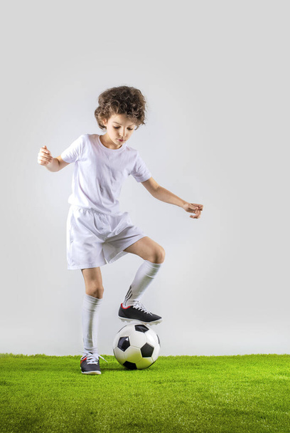 Junior soccer player kicking a ball isolated on gray background - Φωτογραφία, εικόνα