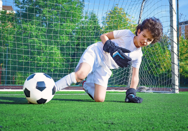 Young boy or kid plays soccer or football sports for exercise and activity. The boy goalkeeper has trying to hit the ball with his foot - Фото, изображение