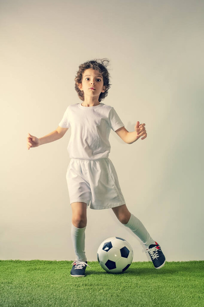 Junior soccer player kicking a ball isolated on gray background - Valokuva, kuva