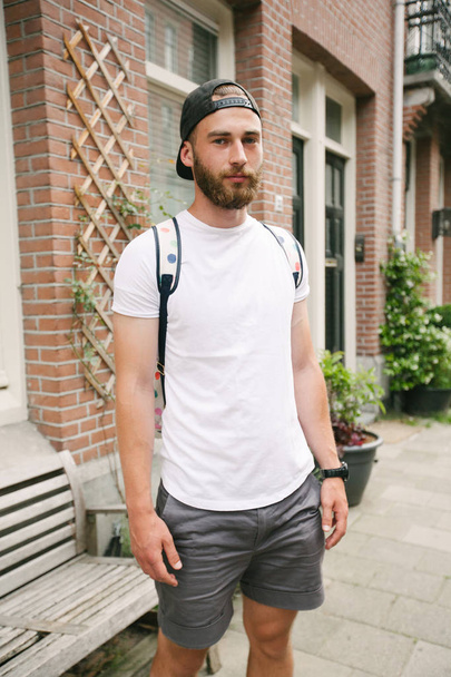 Hipster handsome male model with beard wearing white blank t-shirt and a baseball cap with space for your logo or design in casual urban style - Fotografie, Obrázek