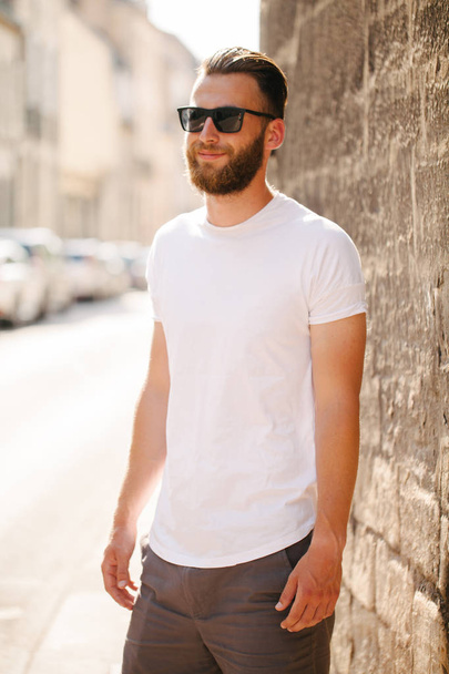 Hipster handsome male model with beard wearing white blank t-shirt and a baseball cap with space for your logo or design in casual urban style - Foto, Bild