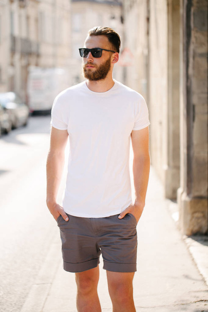 Hipster handsome male model with beard wearing white blank t-shirt and a baseball cap with space for your logo or design in casual urban style - Fotoğraf, Görsel
