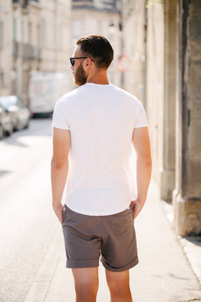 Hipster handsome male model with beard wearing white blank t-shirt and a baseball cap with space for your logo or design in casual urban style - Foto, Imagem