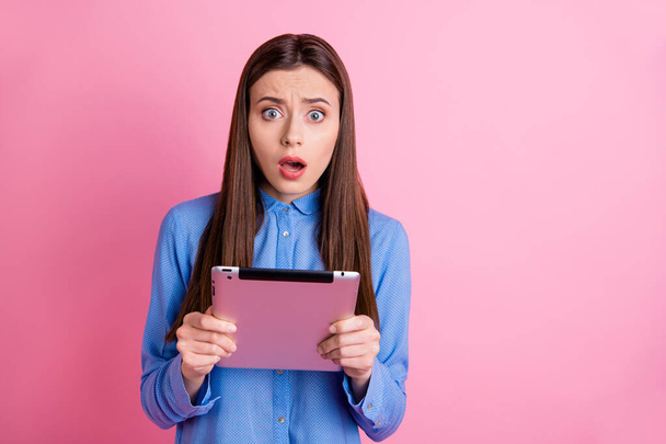 Photo of beautiful disappointed dissatisfied sweet attractive influencing blogger receiving negative comments holding tablet with hands wearing blue shirt isolated pink pastel color background - Fotografie, Obrázek