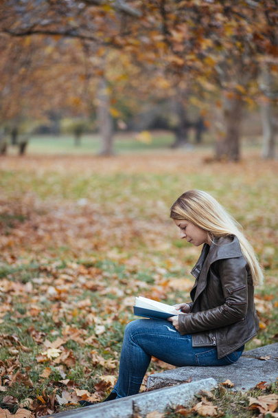 Nuori nainen lukemassa kirjaa puistossa syksyllä
 - Valokuva, kuva