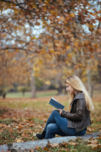 Молода жінка читає книгу в парку восени
 - Фото, зображення