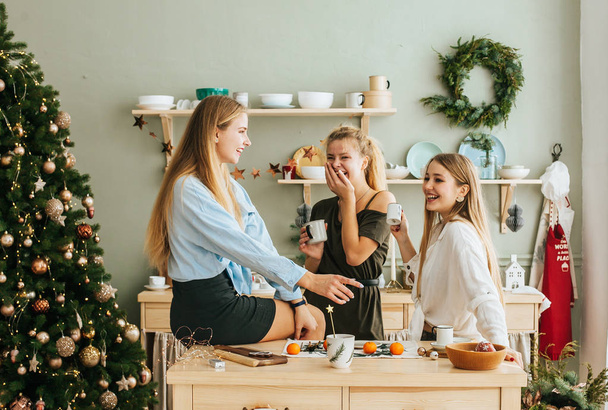 Portrait of laughing girlfriends having christmas snacks in christmas decorated kitchen - 写真・画像
