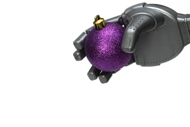 A robot holds a purple Christmas tree decoration in his hand. - Foto, afbeelding