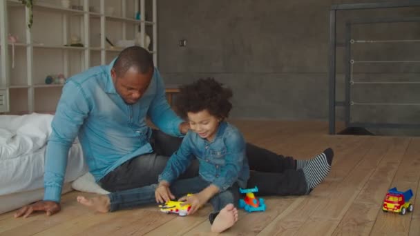 African father and son playing with toys on floor - Materiał filmowy, wideo