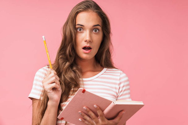 Image closeup of beautiful surprised woman wearing striped t-shirt looking at camera while holding diary and pencil - Fotó, kép