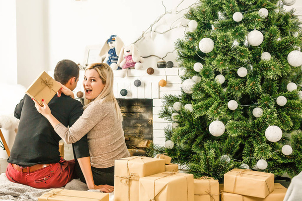Ładny love para siedzi na dywanie przed kominkiem. Kobieta i mężczyzna obchodzi Boże Narodzenie - Zdjęcie, obraz