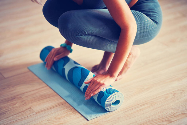 Молода жінка котиться йога килимок вдома
 - Фото, зображення