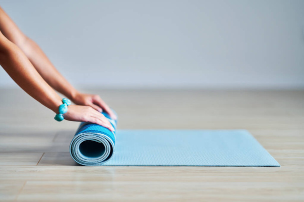 Young woman rolling yoga mat at home - 写真・画像