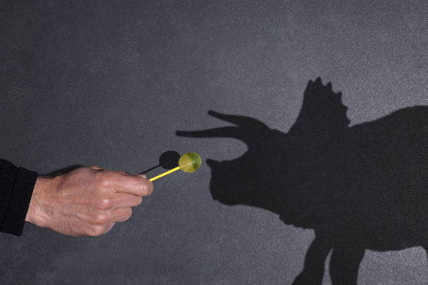 Смешная концепция домашнего животного: рука человека с леденцом в руках и предложение его доисторической тени животного - копировальное место для вашего текста
 - Фото, изображение