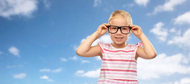 smiling little girl in glasses over sky background - Foto, afbeelding
