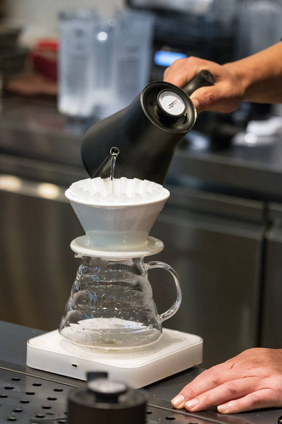 Barista αρσενικό χέρι ρίχνει ζεστό νερό σε ένα σταγονόμετρο για να κάνει καφέ φίλτρο - Φωτογραφία, εικόνα