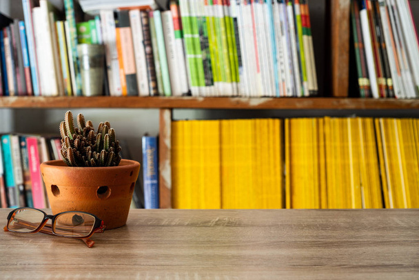 本棚を背景にテーブルの上にグラスと鉢植えのサボテン、スタイルのミニマリストの概念. - 写真・画像