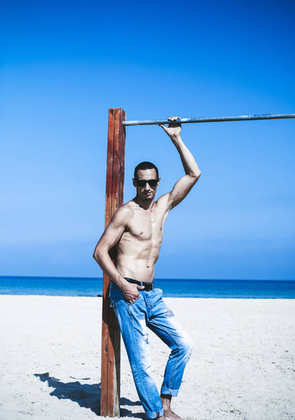 young muscular man resting and posing on the beach. Wearing sunglasses - Foto, Imagem