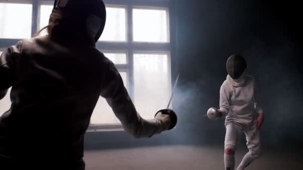 Two young women having training in a fencing duel in the smoky studio - Footage, Video