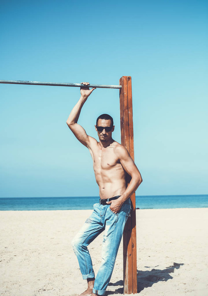 young muscular man resting and posing on the beach. Wearing sunglasses - Valokuva, kuva