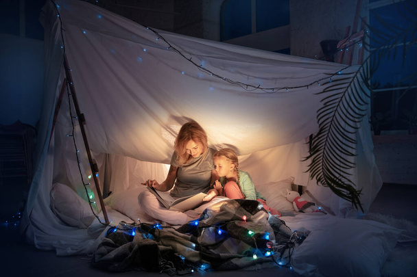 Mother and daughter sitting in a teepee, reading stories with the flashlight - Фото, зображення
