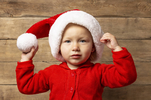 Μικρό παιδί στον Άγιο Βασίλη καπέλο σε ξύλινο φόντο. Χριστούγεννα έννοια, οικογενειακές διακοπές - Φωτογραφία, εικόνα
