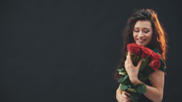 Cute curly brunette girl standing, smelling red roses. Courier is walking on the background with clipboard. - Video
