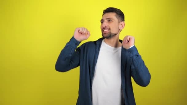 A young man in a white T-shirt and blue shirt is dancing with a smile on a yellow background. 4k footage - Footage, Video