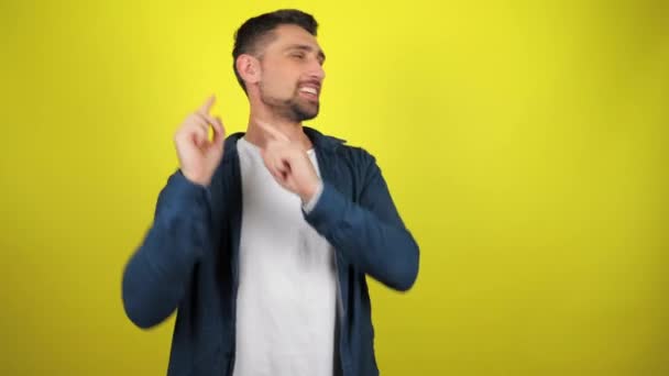 A young man in a white T-shirt and blue shirt is dancing and smiles on a yellow background with copy space. 4k footage - Footage, Video