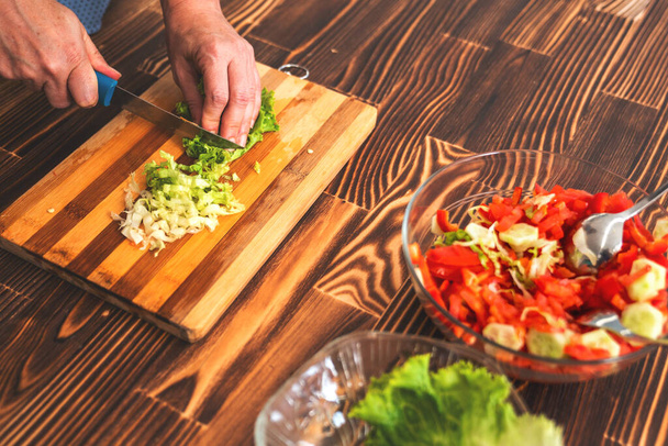 Young woman is cutting lettuce on cutting board for salad - 写真・画像