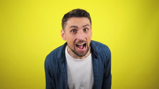 A young man in a blue shirt and white T-shirt is looks at camera and screaming, growls like a lion. Yellow background with copy space. 4k slowmotion footage - Footage, Video