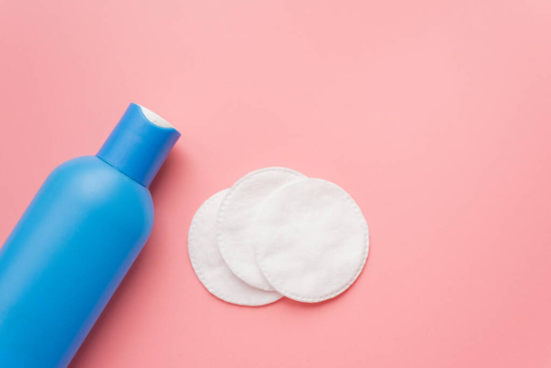 Cleansing and moisturizing facial lotion in blue packaging and cotton pads on a pink pastel background. The concept of home skin care. Copyspace - Photo, Image