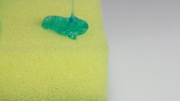 Blue dish washing liquid gel is pouring on yellow sponge on white background  - Filmati, video