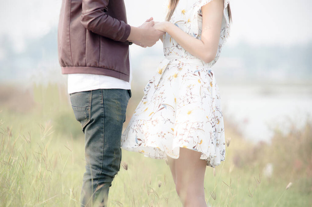 若いカップルは美しい牧草地と自然の背景と握手するスタンドします。. - 写真・画像