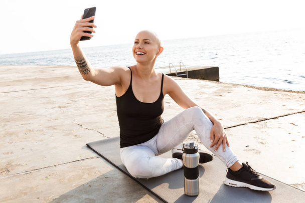 Image of smiling bald woman taking selfie photo on cellphone - Фото, изображение