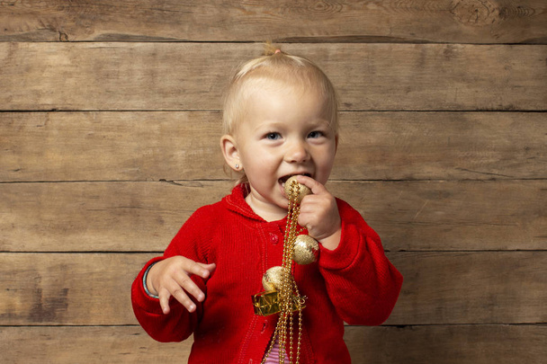 Klein kind speelt met kerstversieringen op een houten achtergrond. Kerstconcept, familievakanties - Foto, afbeelding