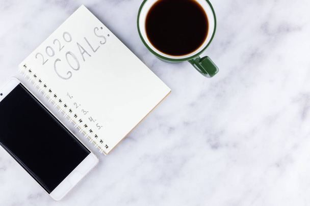 2020 new year goals, plan, action text on notepad on white marble background. 2020 goals on blank note paper with copy space for text. Cup of coffee and smartphone over marble background - Zdjęcie, obraz