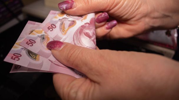 Volwassen leeftijd vrouw onderdak geld aan de kassa, Mexicaanse peso 's - Foto, afbeelding