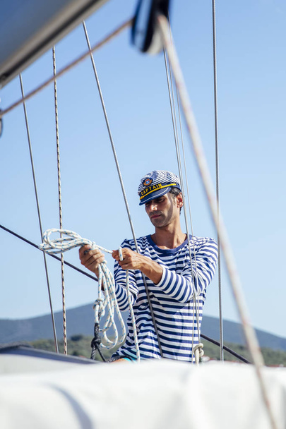 Hezký mladý muž s kapitánem čepice na plachetnici na moři v suuny den - Fotografie, Obrázek