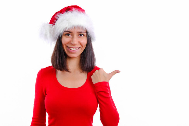 Wow fantastic tell more. Intrigued fascinated young woman is smiling in red christmas Santa hat. Emotional girl stands pointing up finger see incredible good promo sale. On white - Foto, immagini