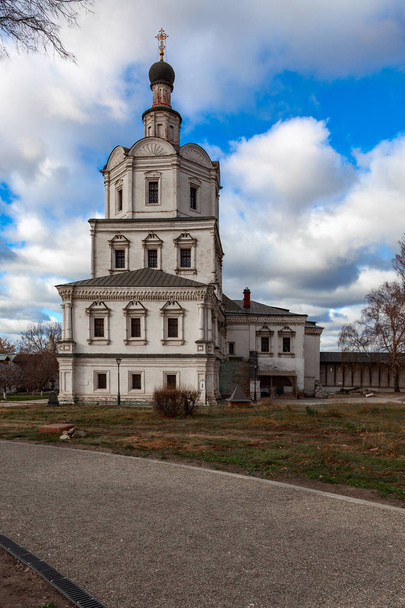An ancient Orthodox church on the territory of the Andrei Rublev Museum in Moscow against a cloudy sky. In the foreground is a gravel path - Fotó, kép