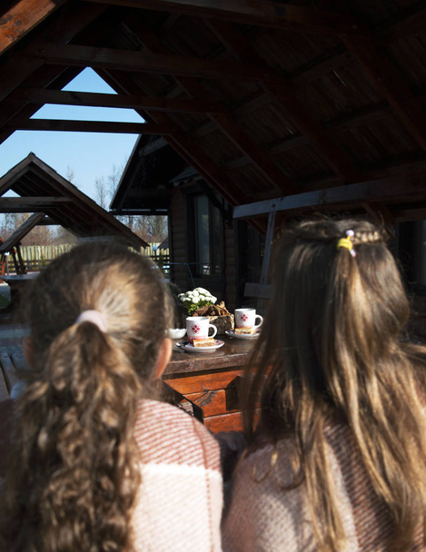 Horký čaj ve dvou bílých šálcích a koláčky u dřevěného stolu. Přední pohled je rozmazané dvě dívky v kostkovaném.  - Fotografie, Obrázek