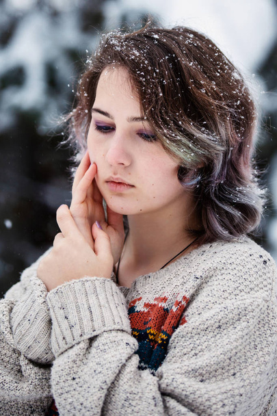 A girl of Caucasian appearance in a sweater and jeans a background of snowy trees. Snowy winter day. A fun walk. Pensive young girl. - Фото, зображення
