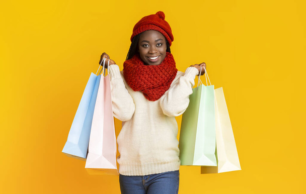 Happy black shopaholic woman with shopping bags over yellow background - Fotó, kép