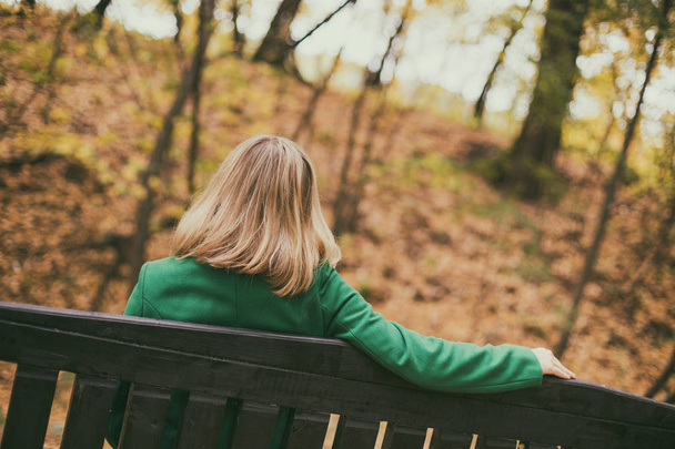 Samotna kobieta siedząca na ławce w parku. - Zdjęcie, obraz