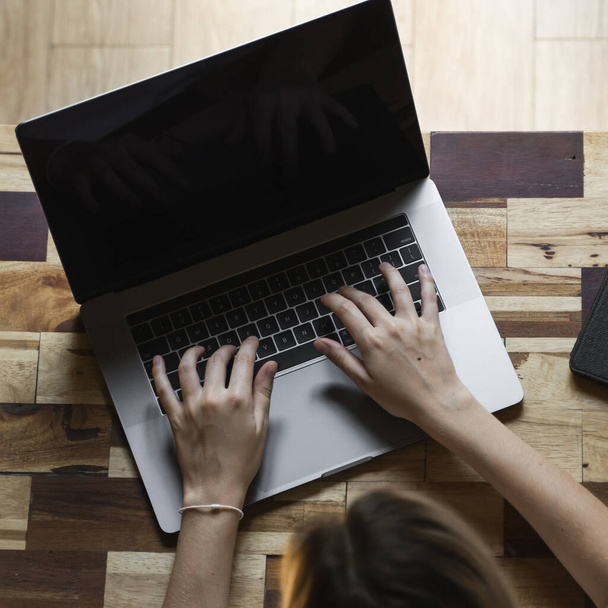 Οι γυναίκες δακτυλογραφούν τα χέρια στην επάνω όψη πληκτρολογίου φορητού υπολογιστή. Μελέτη και εργασία σε απευθείας σύνδεση, ελεύθερος επαγγελματίας. Αυτοαπασχολούμενη ή ανεξάρτητη γυναίκα, κορίτσι που εργάζεται με το laptop της κάθεται σε ξύλινο τραπέζι με τηλέφωνο και ηλεκτρονικό αναγνώστη. - Φωτογραφία, εικόνα