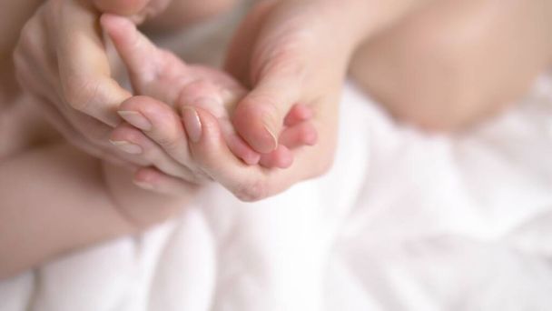 Τα γυναικεία χέρια κάνουν μασάζ στο μωρό στο κρεβάτι. κοντινό πλάνο - Φωτογραφία, εικόνα